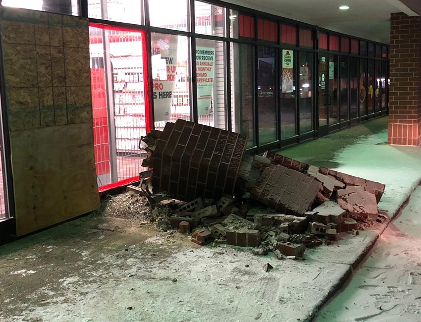 A broken brick pillar with boarded up windows in a strip mall